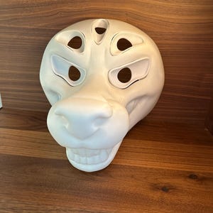 May include: White unpainted furry animal mask with five holes for eyes and nose. The mask is made of a smooth, hard material and has a realistic expression.