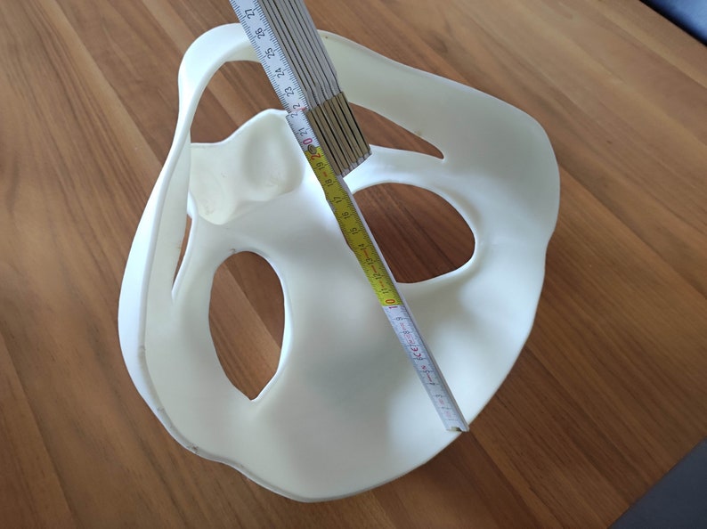 May include: White plastic mold with two large holes and a smaller hole in the center. A yellow measuring tape is placed across the mold, with the numbers 10, 11, 12, 13, 14, 15, 16, 17, 18, 19, 20, 21, 22, 23, 24, 25, 26, 27 visible.
