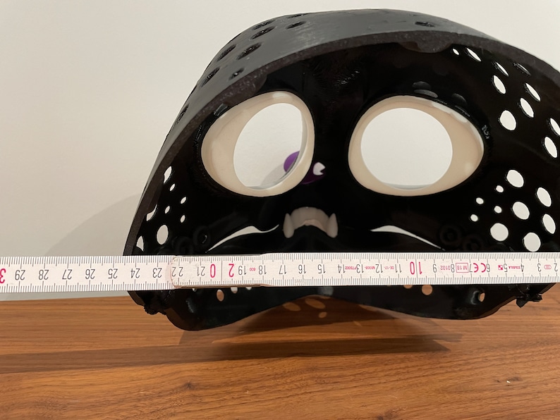 May include: Black plastic mask with white eye holes and a white mouth. The mask is 50.8 cm wide.