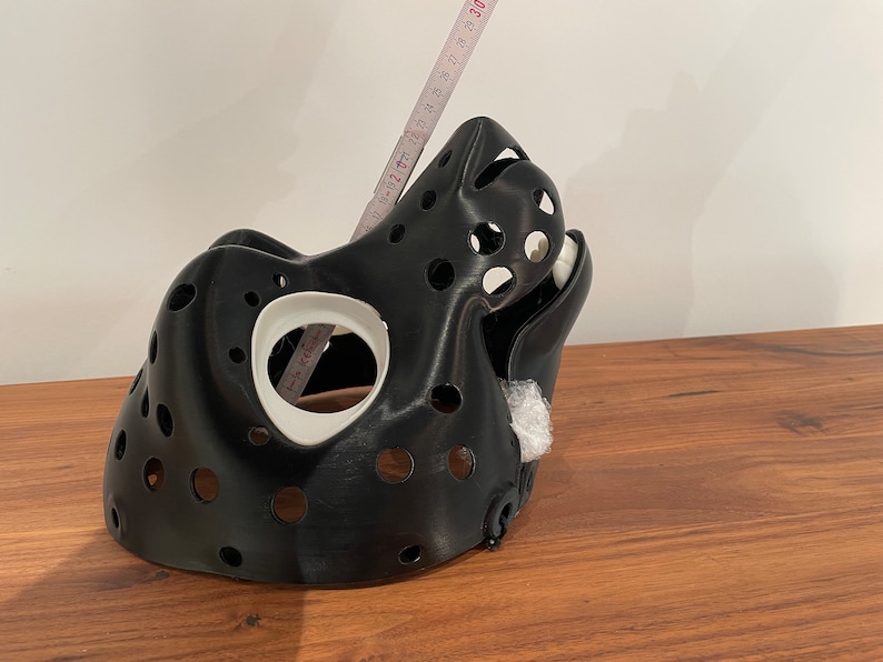 May include: A black 3D printed mask with a white interior and multiple holes. The mask is shaped like an animal head and has a long snout.