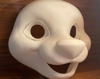 May include: White unfinished furry animal mask with large eyes, a small nose, and a wide open mouth. The mask is made of a smooth, hard material.