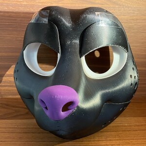May include: A black furry animal mask with white eye holes and a purple nose. The mask is made of a smooth, textured material.