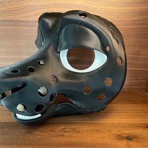 May include: A black and white furry animal mask with a white eye socket and a black nose. The mask is made of a hard plastic material and has a lot of holes in it.