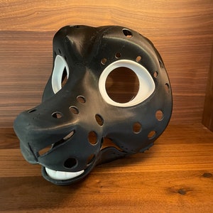 May include: Black and white furry animal mask with holes for eyes and nose. The mask is made of a smooth, hard plastic and has a textured surface.