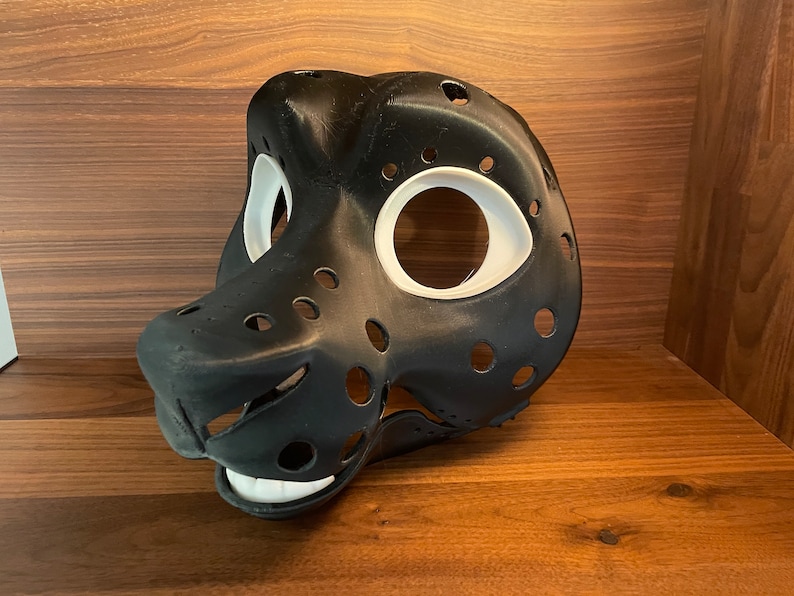 May include: Black and white furry animal mask with holes for eyes and nose. The mask is made of a smooth, hard plastic and has a textured surface.