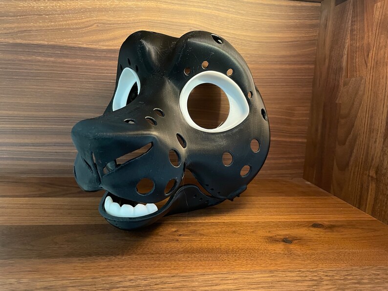 May include: A black and white 3D printed furry mask with holes for eyes and a mouth. The mask is designed to look like an animal head.