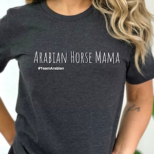 May include: Dark gray t-shirt with the text "ARABIAN HORSE MAMA" in white, with the hashtag "#TeamArabian" underneath. The shirt is a short-sleeved crew neck style.