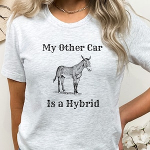 May include: Light gray t-shirt with the text "My Other Car Is a Hybrid" above a black and white illustration of a donkey. The shirt has short sleeves and a crew neck.
