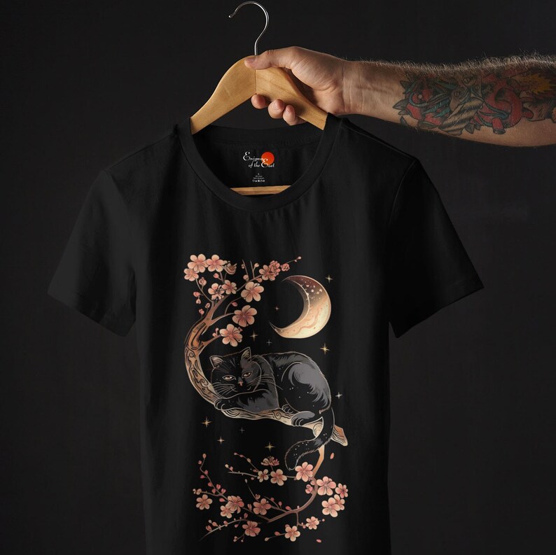 May include: Black t-shirt with a graphic of a black cat sleeping in a cherry blossom tree under a crescent moon. The text "Empress of the Night" is on the shirt.