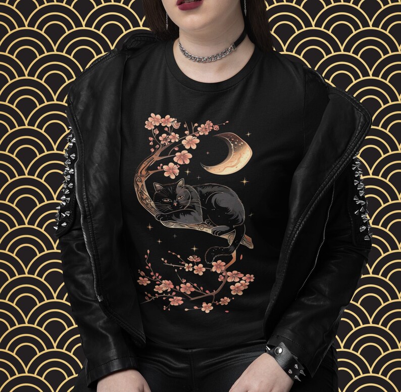May include: Black t-shirt with a graphic of a black cat sleeping on a branch with pink cherry blossoms and a crescent moon.