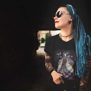 K&ouml;nnte beinhalten: Schwarzes V-Ausschnitt-T-Shirt mit einer Grafik einer Frau in einem Kimono und Schmetterlingen. Der Kimono ist lila und blau. Die Person auf dem Bild tr&auml;gt eine Sonnenbrille und hat blaue Z&ouml;pfe.