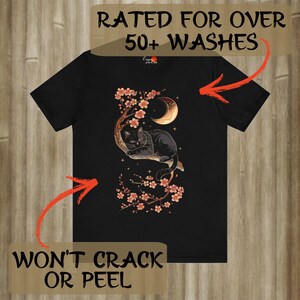 May include: Black t-shirt with a graphic of a black cat sitting in a cherry blossom tree with a crescent moon. The text "Rated for over 50+ washes" and "Won't crack or peel" is on the image.