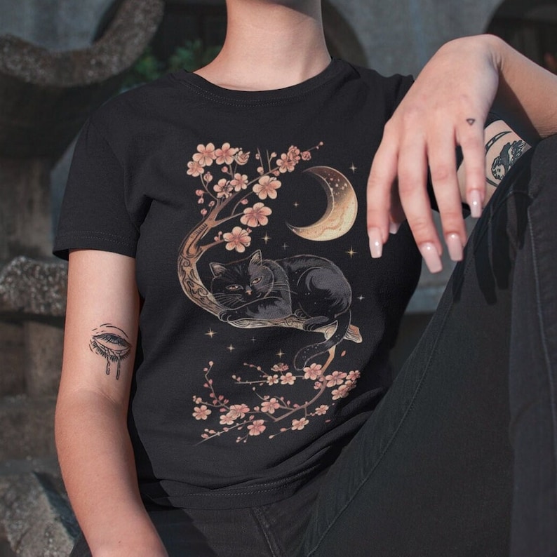 May include: Black t-shirt with a graphic of a black cat sleeping on a branch of a cherry blossom tree with a crescent moon in the background.