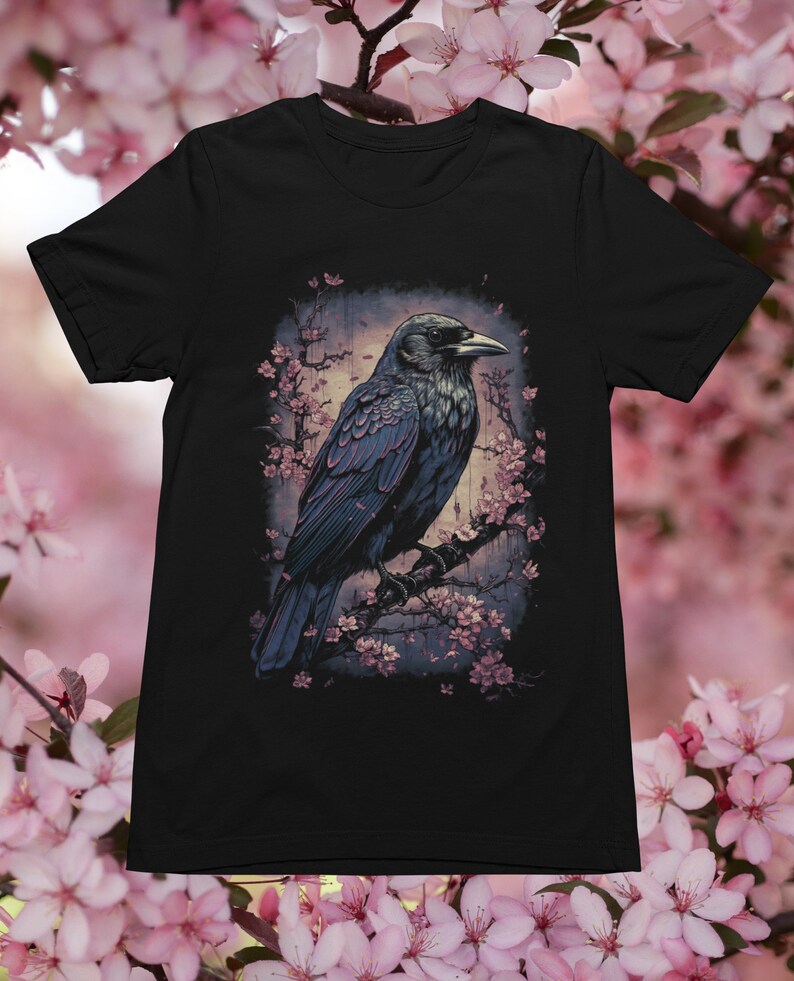 K&ouml;nnte beinhalten: Ein schwarzer Rabe sitzt auf einem Ast mit rosa Bl&uuml;ten. Der Rabe blickt nach rechts und hat einen dunkelblaugrauen K&ouml;rper mit einem schwarzen Schnabel. Der Hintergrund ist ein verschwommenes Bild eines Waldes.