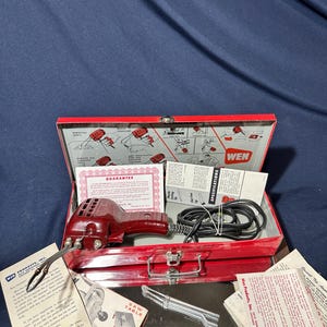May include: A vintage Wen electric soldering tool in a red metal carrying case. The set includes a maroon plastic-bodied tool with a black power cord, a guarantee certificate, a specifications manual, and various paper inserts with product information.