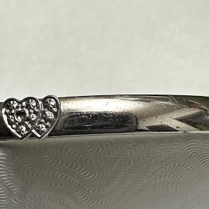 May include: Silver bracelet featuring a double heart design. The hearts are textured and detailed, adding visual interest to the piece. The bracelet has a simple, elegant design, suitable for everyday wear.