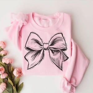 May include: A pink sweatshirt with a black and white illustration of a bow on the front.