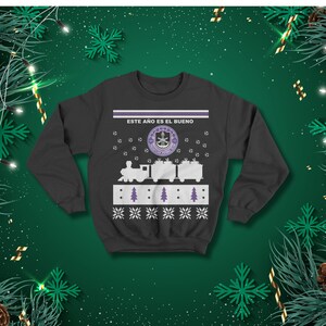 May include: Dark grey sweatshirt with a festive design. The design features a train, Christmas trees, snowflakes, and the text "ESTE A&Ntilde;O ES EL BUENO". The sweatshirt has a crew neck and long sleeves.