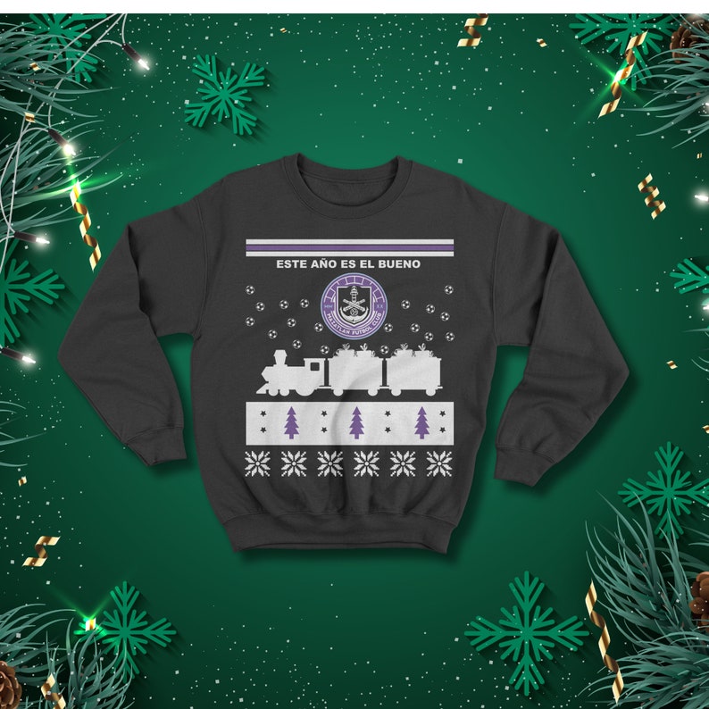 May include: Dark grey sweatshirt with a festive design. The design features a train, Christmas trees, snowflakes, and the text "ESTE A&Ntilde;O ES EL BUENO". The sweatshirt has a crew neck and long sleeves.