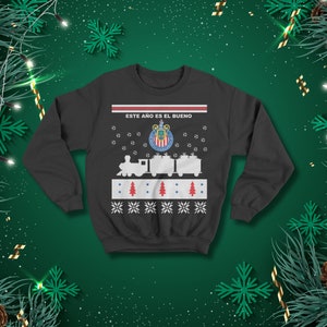 May include: Dark grey sweatshirt featuring a festive design. The design includes a train, soccer balls, Christmas trees, snowflakes, and the text "ESTE A&Ntilde;O ES EL BUENO" above the team logo. Ideal for the holiday season.