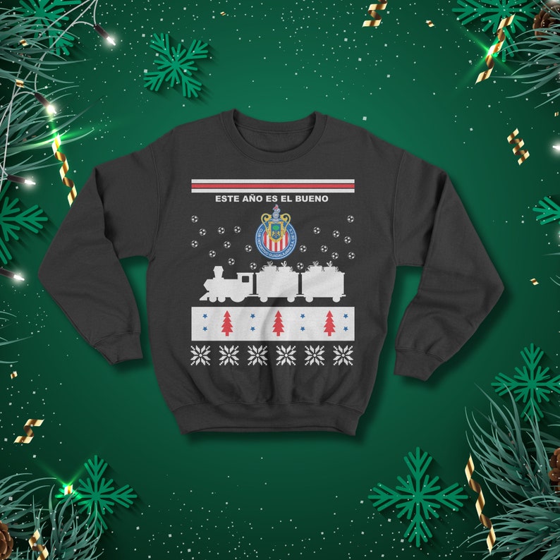 May include: Dark grey sweatshirt featuring a festive design. The design includes a train, soccer balls, Christmas trees, snowflakes, and the text "ESTE A&Ntilde;O ES EL BUENO" above the team logo. Ideal for the holiday season.