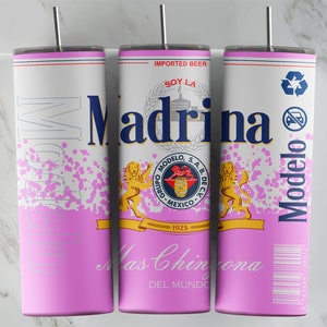 Puede incluir: Un vaso de acero inoxidable rosa y blanco con un diseño que presenta el logotipo de la cerveza Modelo, el texto "Soy La Madrina" y un león. El vaso tiene un patrón de salpicaduras rosa y un código de barras en blanco y negro.