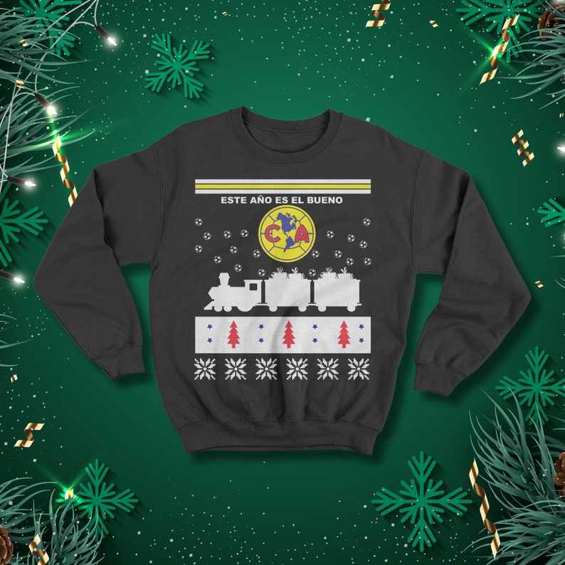 May include: Dark grey sweatshirt with a festive design. The design includes a train carrying gifts, footballs, snowflakes, and the text "ESTE A&Ntilde;O ES EL BUENO" above a team logo. A holiday-themed apparel item.