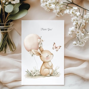 May include: A greeting card featuring a watercolour illustration of a rabbit holding a pink balloon. A butterfly and flowers are also depicted. The words "Thank You!" are written at the top. The card is on a white background.