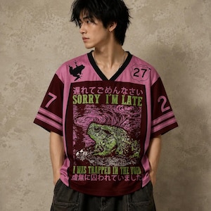 May include: A pink and maroon V-neck jersey featuring a graphic of a green frog, the text "SORRY I'M LATE" and "I WAS TRAPPED IN THE VOID," Japanese characters, the number 27 in a shield, and the numbers 7 and 2 on the sleeves with striped detailing.