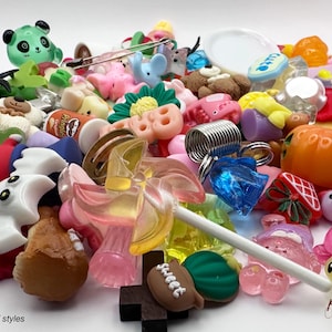 May include: A selection of colourful charms and embellishments in various shapes, including a green panda, a pink flower, and a football with the word "sweet". The image includes a lollipop and the text "example of styles".