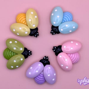 May include: Five colorful ladybug-shaped buttons with white polka dots. The buttons are in shades of yellow, green, blue, pink, and purple.