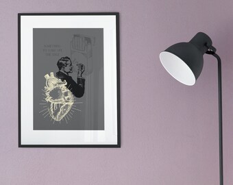 May include: A framed print with a black frame and a gray background. The print features a vintage illustration of a human heart with a man smoking a cigarette. The text "Something to fall off the edge" is printed in white.