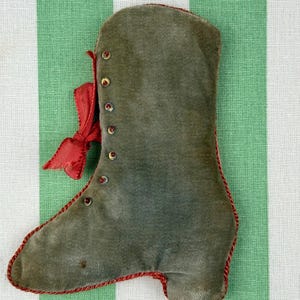Puede incluir: Adorno en forma de bota verde oliva con ribete rojo y lazo de cinta roja. La bota tiene pequeños botones rojos decorativos y está hecha de un material suave y aterciopelado. Para decoración de temporada.