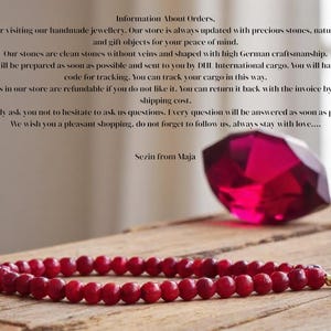 May include: A red gemstone bracelet with gold accents. The bracelet is made of small, round beads and is lying on a wooden surface. A large, red gemstone is in the background.