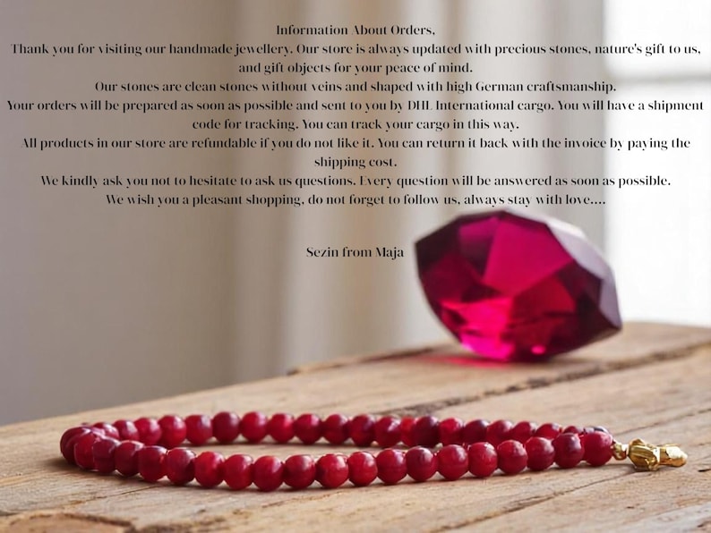 May include: A red gemstone bracelet with gold accents. The bracelet is made of small, round beads and is lying on a wooden surface. A large, red gemstone is in the background.