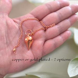 Op de afbeelding: Een koperen of verguld slinger met een puntige punt en een ketting. De slinger wordt in een hand gehouden.