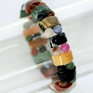 May include: A colourful beaded bracelet featuring a variety of stones, including green, red, black, white, and yellow. The bracelet is made from natural stones and is strung on an elastic cord.