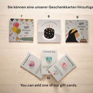 May include: A set of greeting cards with different birthday designs. The cards feature colourful balloons, a birthday cake, and a person blowing out candles. The cards are displayed on a wooden surface. You can add one of our gift cards.