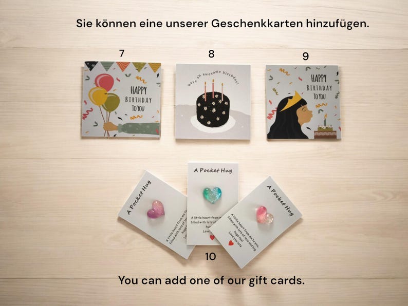 May include: A set of greeting cards with different birthday designs. The cards feature colourful balloons, a birthday cake, and a person blowing out candles. The cards are displayed on a wooden surface. You can add one of our gift cards.