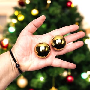 Peut inclure: Deux boules de Noël dorées brillantes dans la paume d'une main.