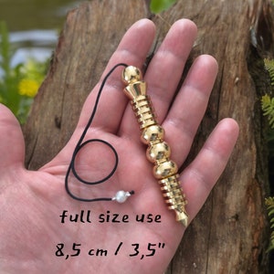 Può includere: Un pendolo in metallo dorato con un cordino nero e una perla bianca. Il pendolo è lungo 8,5 cm / 3,5 pollici. Il testo "full size use" e "8,5 cm / 3,5" è scritto sotto il pendolo.