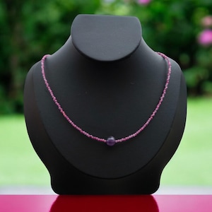 Könnte beinhalten: Eine Halskette aus rosafarbenen Edelsteinen mit einem einzelnen Anhänger aus violettem Edelstein auf einem schwarzen Präsentationsständer.
