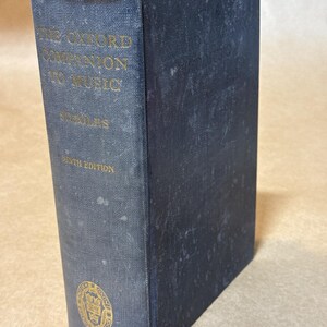 May include: A vintage, hardcover book titled "The Oxford Companion to Music" by Percy A. Scholes, Sixth Edition. The book has a dark blue cover with gold lettering and a gold emblem. The book is in good condition.