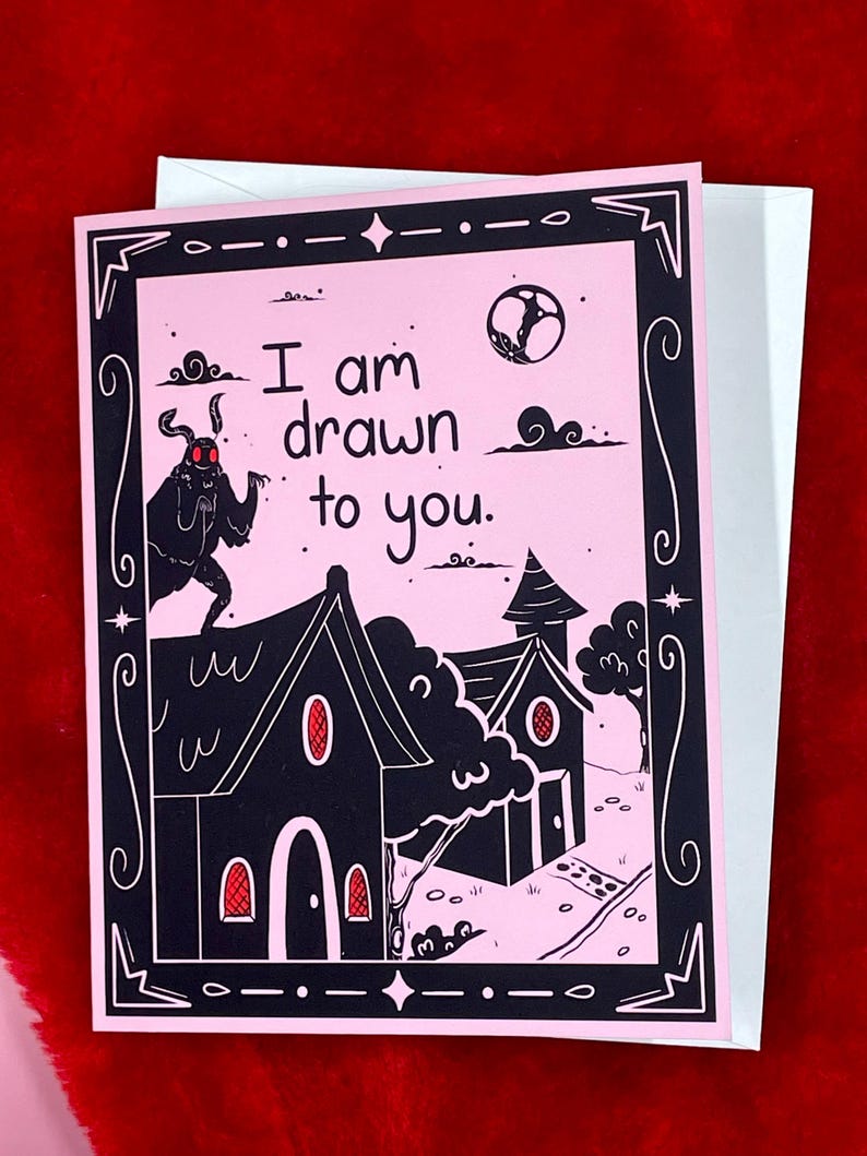 May include: A pink greeting card with a black and white illustration of a moth, two houses, and a moon. The text on the card reads "I am drawn to you."