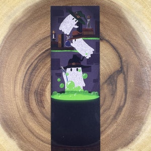 May include: A bookmark featuring a cartoon illustration of three ghosts wearing witch hats. The ghosts are in a dark room with a cauldron of green bubbling liquid. The top ghost is flying, the middle ghost is reaching into the cauldron, and the bottom ghost is stirring the liquid with a wand.