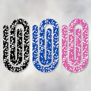 May include: Three abstract, U-shaped designs in black, blue, and pink, each with a white, speckled pattern. The shapes are arranged vertically against a light gray background, resembling notebook paper.