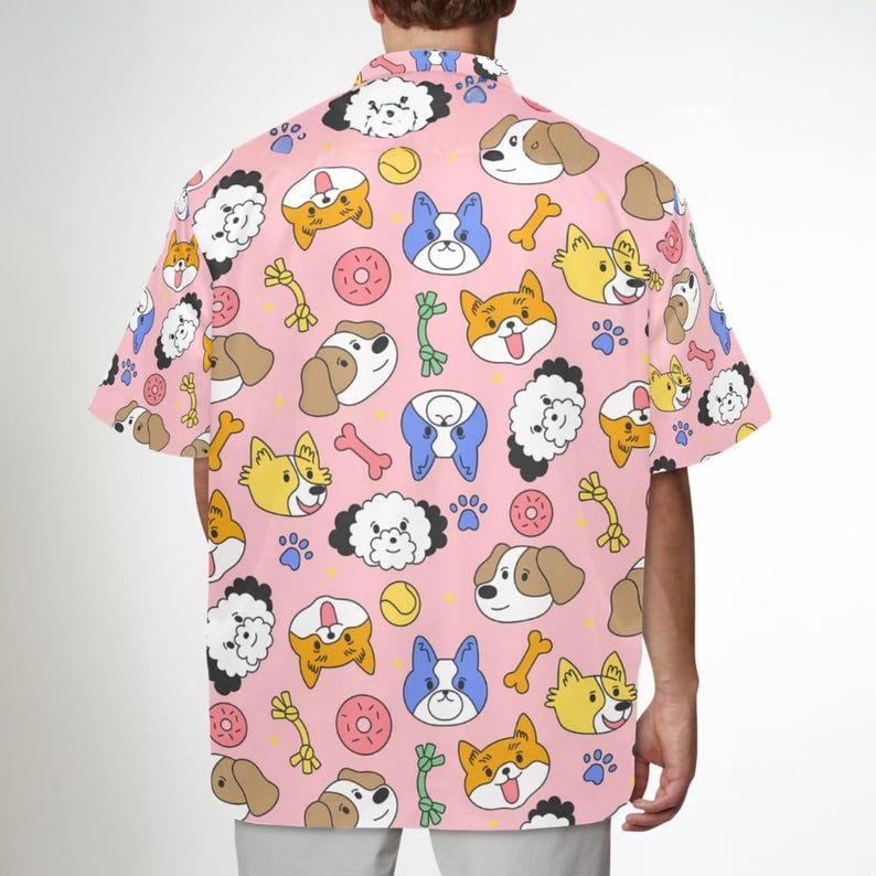 Pu&ograve; includere: Una camicia rosa con bottoni e un motivo ripetuto di cani dei cartoni animati, ossa e giocattoli per cani. I cani sono di vari colori e pose.