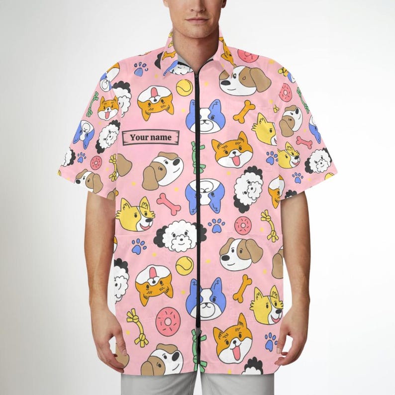 Pu&ograve; includere: Camicia rosa a maniche corte con un motivo di cani dei cartoni animati, ossa e impronte di zampe. La camicia ha una chiusura a zip e una tasca sul petto sinistro con il testo "Your name".