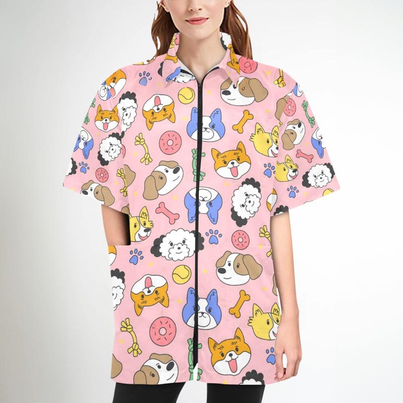 Pu&ograve; includere: Camicia rosa a maniche corte con chiusura a zip e un motivo di cani dei cartoni animati, ossa e ciambelle.