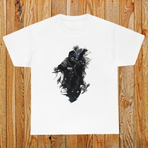 Op de afbeelding: Wit T-shirt met een zwart-witte grafische print van een gekapte figuur die een wapen vasthoudt. De figuur is omringd door een zwart-wit abstract ontwerp.